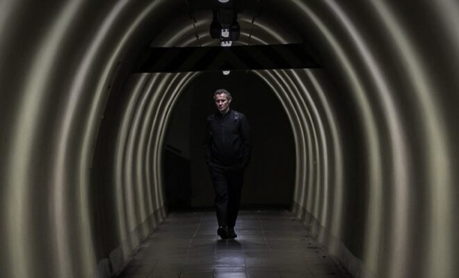 Kadr z filmu. Mężczyzna w czarnym ubraniu, w słabo oświetlonym tunelu.