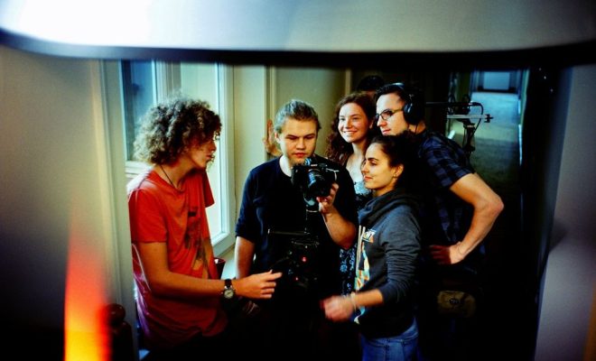 Zdjęcie młodzieży biorącej udział w warsztatach filmowych. Grupa trzyma kamerę i rozmawia.