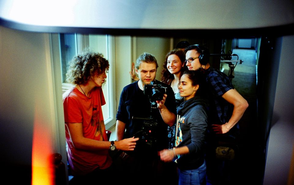 Zdjęcie młodzieży biorącej udział w warsztatach filmowych. Grupa trzyma kamerę i rozmawia.