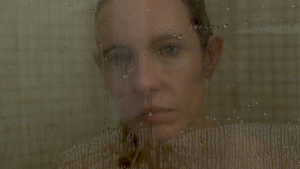 Kobieta z mokrymi włosami za zaparowaną szybą kabiny prysznicowej.
