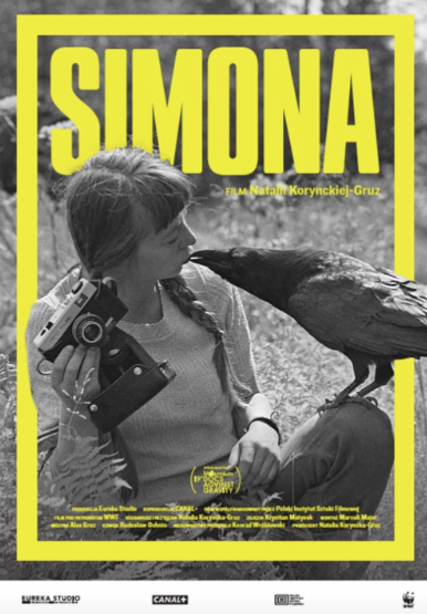 Plakat promujący film. Młoda kobieta z dwoma warkoczami dotyka ustami dzioba ptaka, siedzącego na jej kolanie. W ręce trzyma aparat fotograficzny.