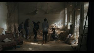 Zrujnowane wnętrze domu. Kilka kobiet sprząta piach i gruz, zalegające pod ścianami na podłodze.