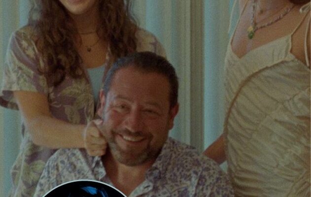 Kadr z filmu. Mężczyzna w kwiecistej koszulki siedzi, przed nim stoi tort na stole. Za mężczyzną stoją dwie młode, śmiejące się kobiety w sukienkach.