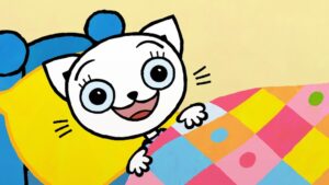 Kadr z filmu animowanego. Biała kicia w łóżeczku, uśmiecha się, leżąc od kolorową kołdrą.