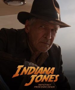 Grafika promująca film. Indiana Jones w brązowym kapeluszu, w ciemnej marynarce, patrzy uważnie w swoją prawą stronę.