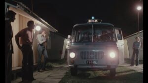 Samochód milicyjny, otoczony przez grupę mężczyzn, nocą. Kadr z filmu.