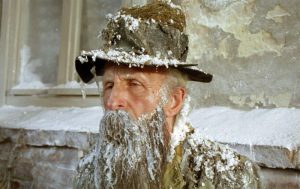 Kadr z filmu. Portret. Starszy mężczyzna z siwą brodą, w kapeluszu, pokryty soplami, śniegiem, wodorostami.