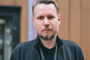 Młody mężczyzna (Kuba Mikurda) w bluzie, na szyi smycz festiwalu MDAG.