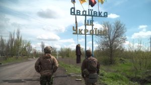 Fotografia. Dwóch żołnierzy stoi zwróconych tyłem do obiektywu, w tle napis po ukraińsku, na nim wisi kukła.