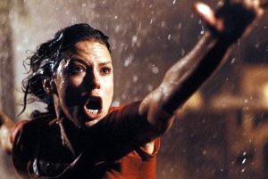 kadr z filmu. Kobieta w ciemnych mokrych włosach, w deszczu, krzyczy, wyciągając przed siebie rękę.