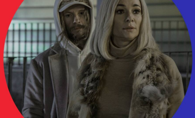 Kadr z filmu INNI LUDZIE. Dojrzała kobieta w blond włosach, futrze, patrzy w bok. Za nią młody mężczyzna w kapturze i długich włosach.