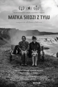 plakat. czarno-białe zdjęcie. Starsza kobita w spódnicy, ciemnym odzieniu wierzchnim, kapelusiku z welonem siedzi na ławce, obok starszy mężczyzna z brodą, w szarej codziennej odzieży. Trzymają ręce na kolanach. Siedzą na ławce na trawniku; w tle widać morze i rozbijające się o brzeg wysokie fale.