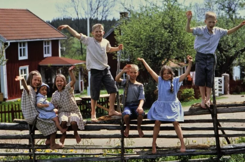 grupa dzieci na drewnianym płocie, 6 osób. w tle wiejskie szwedzkie domy.