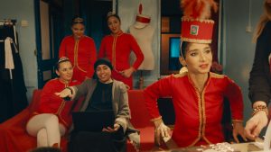 kadr. 4 kobiety w czerwonych strojach, czerwonych czapkach. W centrum starsza kobieta, obrana na czarno, z zasłoniętymi włosami.