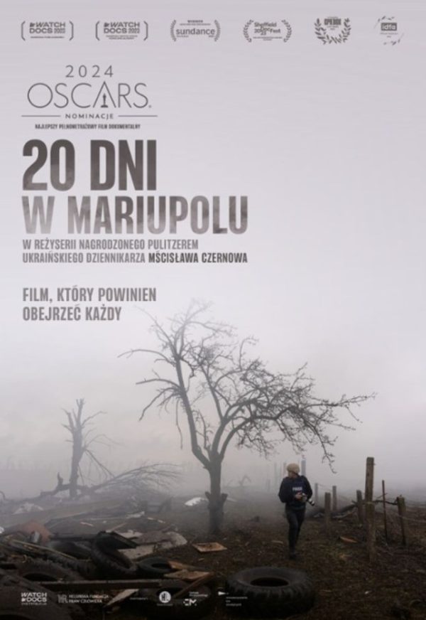 plakat. krajobraz, mgła. drzewo, jakieś śmieci typu opony, obok mężczyzna ubrany w ciemne obranie z aparatem fotograficznym