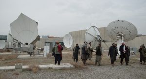 Pomiędzy talerzami anten satelitarnych rozstawionych na placu otoczonym murem idzie grupa mężczyzn w turbanach i tradycyjnych, afgańskich strojach. Część z nich jest uzbrojona.
