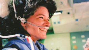 kobieta astronautka, uśmiechnięta, z słuchawkami na uszach i mikrofonem. Ma ciemne, bujne włosy. Zdjęcie archiwalne.