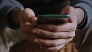 zbliżenie: męskie dłonie trzymające telefon o ciemnozielonej obudowie.