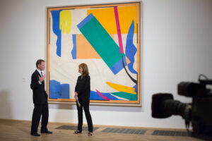 Na ścianie obraz Matisse'a. W prawym roku kadry kamera. Przed kamerą stroją kobieta i mężczyzna, oficjalnie ubrani, rozmawiają.