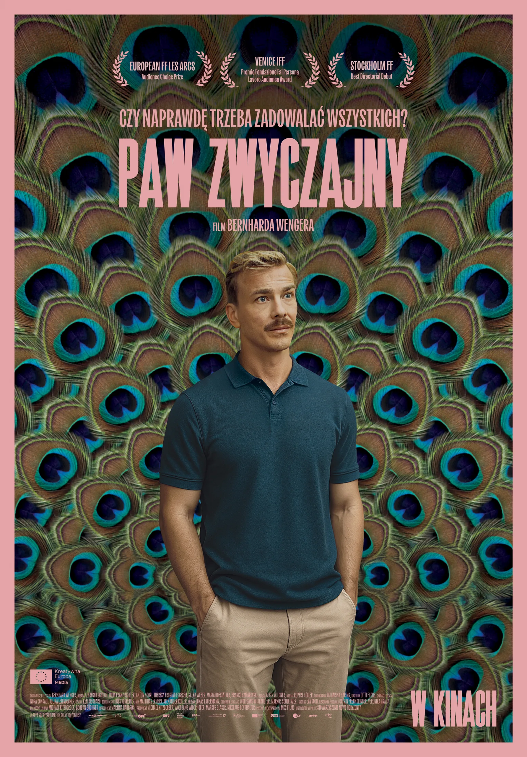 mężczyzna w niebieskiej koszulce i jasnych spodniach na tle grafiki z pawim ogonem