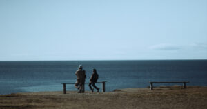 na ławce dwie postaci - dorosła i dziecko. w tle ocean.