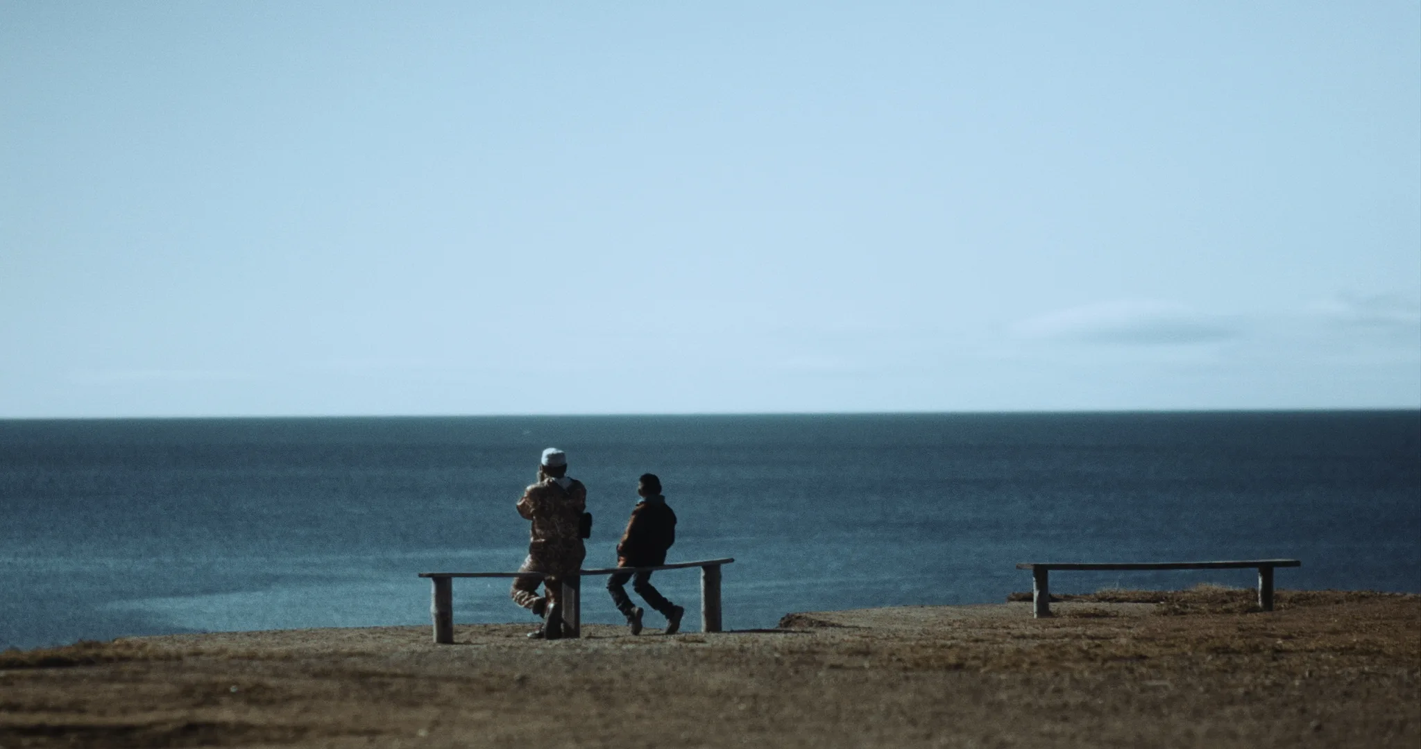 na ławce dwie postaci - dorosła i dziecko. w tle ocean.