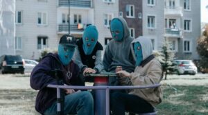 4 chłopaków w niebieskich kominiarkach, bluzach z kapturami, siedzi na karuzeli na miejskim placu zabaw