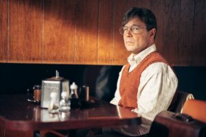 kuchnia. na tle mebla mężczyzna w koszuli, rudej kamizelce, okularach.