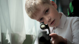 chłopiec, blondyn, w białej koszuli, celuje bronią w stronę obiektywu