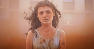 nastolatka z kręconymi długimi włosami, przestraszonym wyrazem twarzy, w brudnej koszulce.