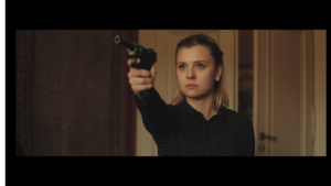 kobieta w czarnej bluzce, blondynka, z upiętymi włosami, celuje rewolwerem w kierunku widza