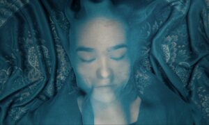 kobieta z zamkniętymi oczyma, przykryta przezroczystą tkaniną