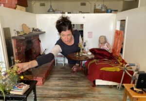 kobieta wychyla się przez małe drzwi miniaturowego pomieszczenia - scenografii. poprawia jakieś meble czy rekwizyty