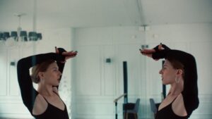 tancerka przy lustrze, wykonuje taneczny gest w rękoma w górze patrząc na swoje odbicie