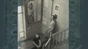 Czarno-biała fotografia: troje ludzi na klatce schodowej, jedna osoba siedzi na schodach, dwie stoją przy ścianie i lustrze.