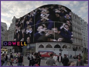 Niewyraźny kadr przedstawiający tłum ludzi przed dużym budynkiem o zaokrąglonej fasadzie.