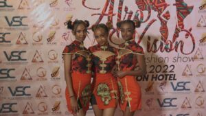 na tle ścianki do zdjęć trzy dziewczyny w pomarańczowych sukienkach uczesane w dwa koczki każda z nich pozują do zdjęcia