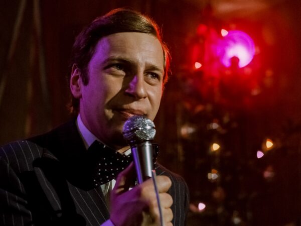 mężczyzna w garniturze, z mikrofonem, oświetlony estradowo