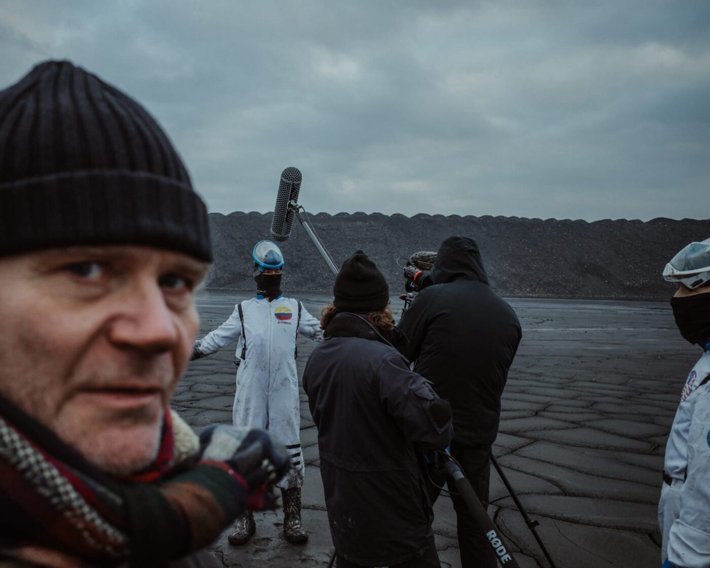 ekipa filmowa z mikrofonem, kamerami na spękanej błotnistej powierzchni. jedna z osób odwraca się i patrzy w kadr.
