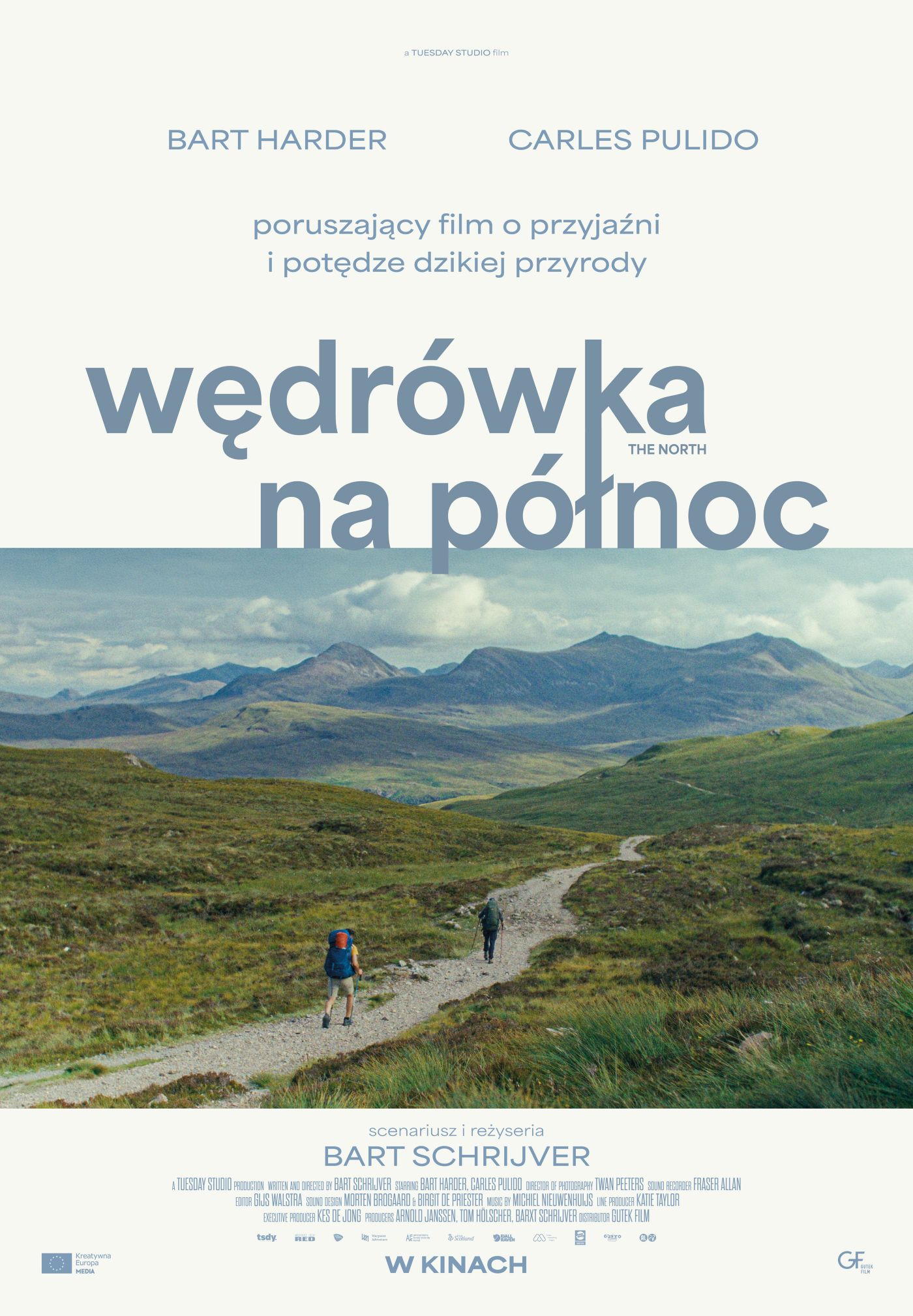 plakat. droga między górami, na niej widać dwóch idących mężczyzn.