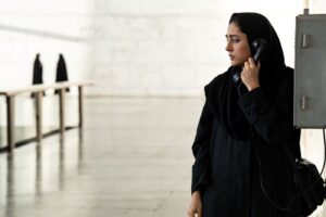 jasne surowe wnętrze, kobieta w czerni, z zasłoniętymi włosami, rozmawia przez telefon stacjonarny