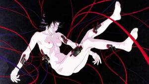 Kadr z filmu „Ghost in the Shell” przedstawiający nagą kobietę unoszącą się w ciemnej przestrzeni, do której ciała podłączone są liczne czerwone i fioletowe przewody.