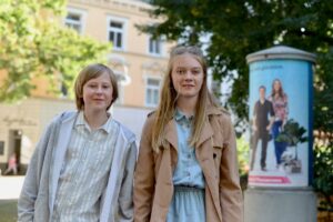 blondyn, w jasnych ubraniach, nastolatek; obok niego wysoka blondynka w beżowym płaszczu i spódniczce