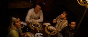 kadr. półmrok, widok z góry na zastawiony jedzeniem stół, 4 osoby z niepokojem patrzą w górę.
